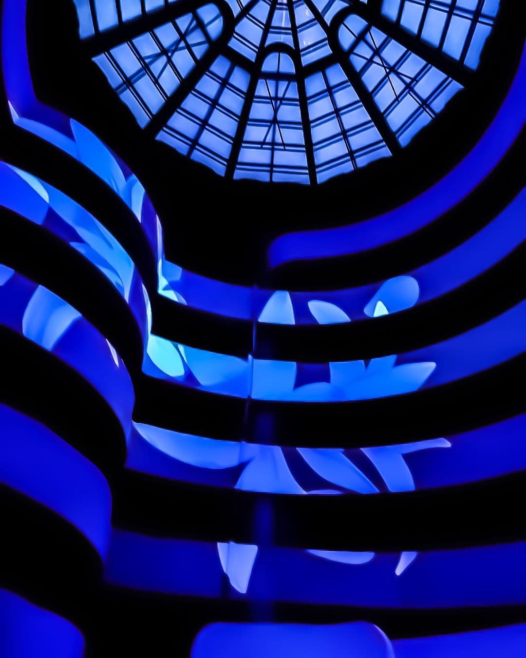 The Guggenheim rotunda's oculus skylight and blue-lit spiral ramps seen from below.