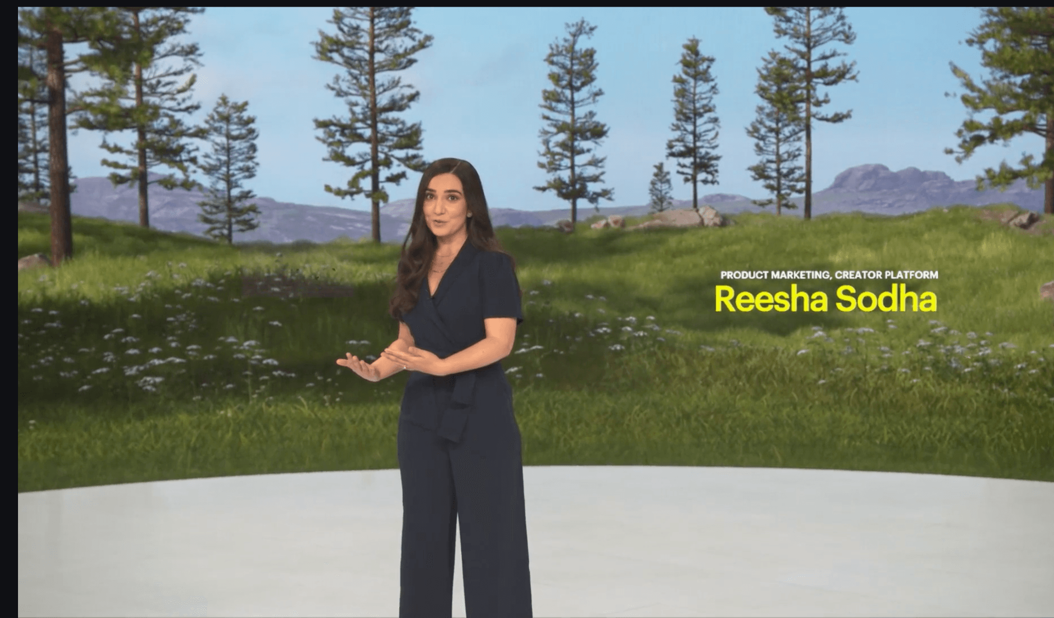 Woman presenting outdoors in front of a screen reading 'Reesha Sodha', trees behind.