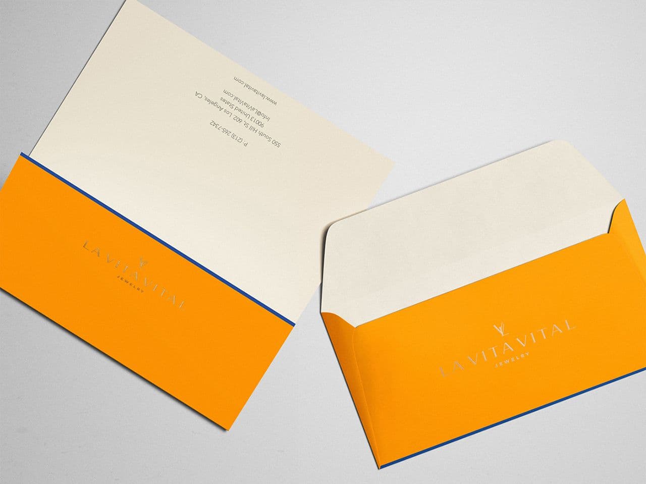 Cream notecard with printed address text beside an orange envelope embossed with the La Vita Vital logo, both edged in navy blue.
