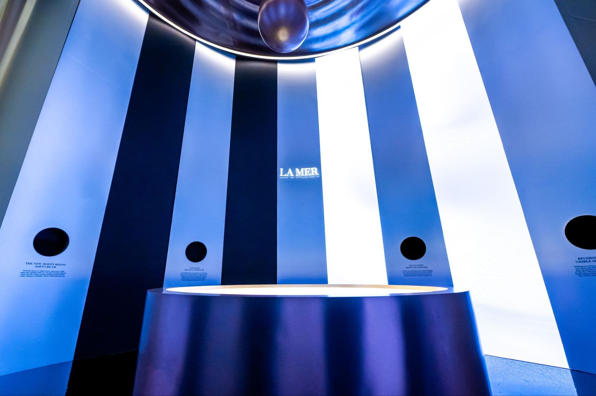 Circular blue-and-white striped ceiling installation with a La Mer logo suspended above a lit floor podium.