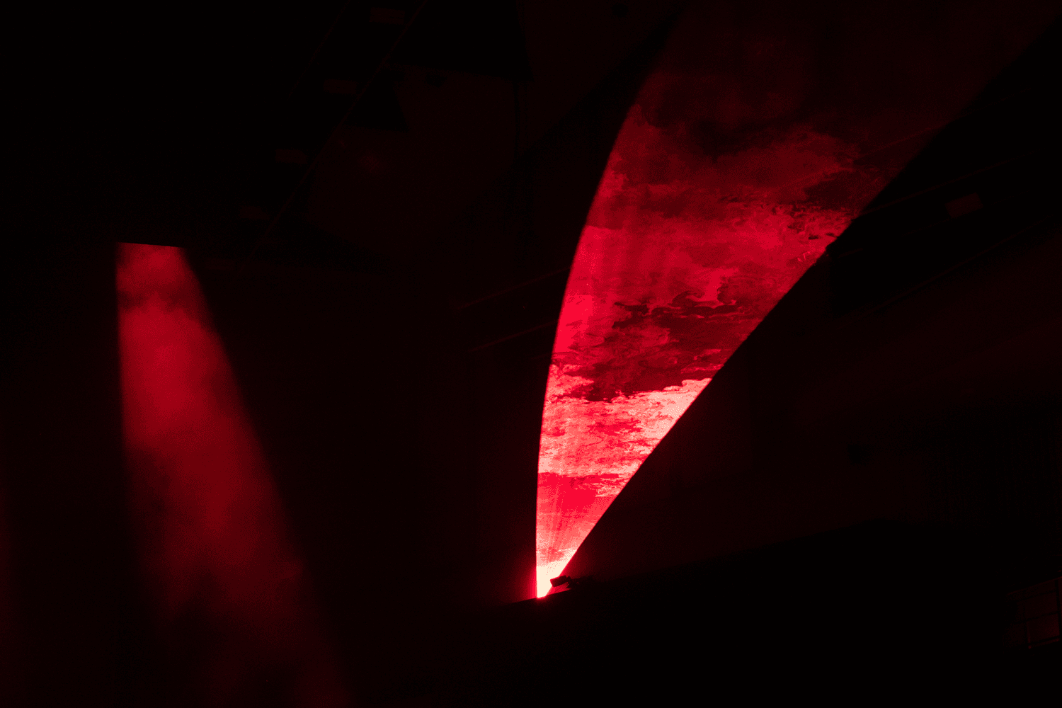 Curved red stage screen lit like a blade or wing shape
