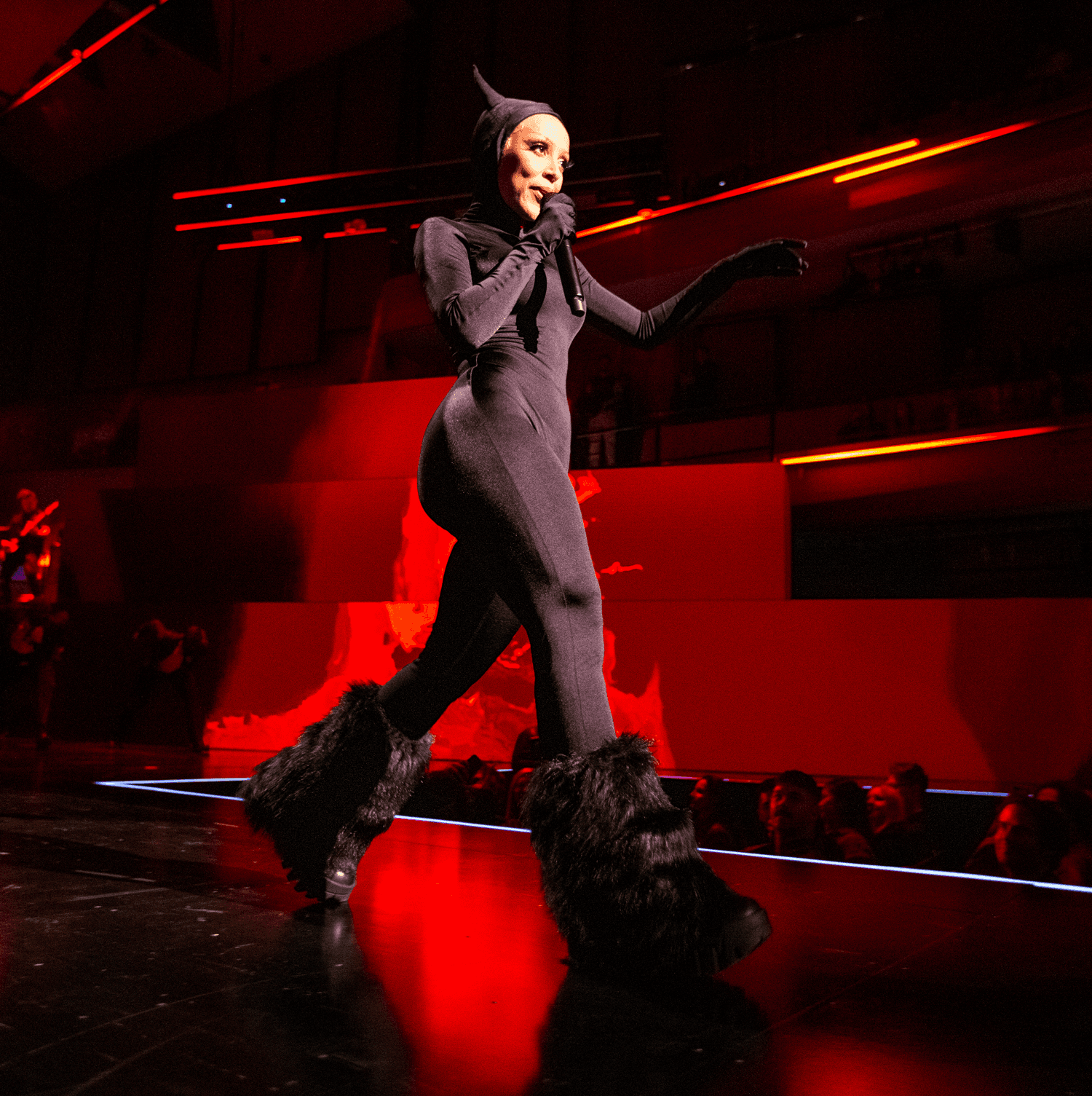 Group of performers in dark outfits posing together under red stage lighting