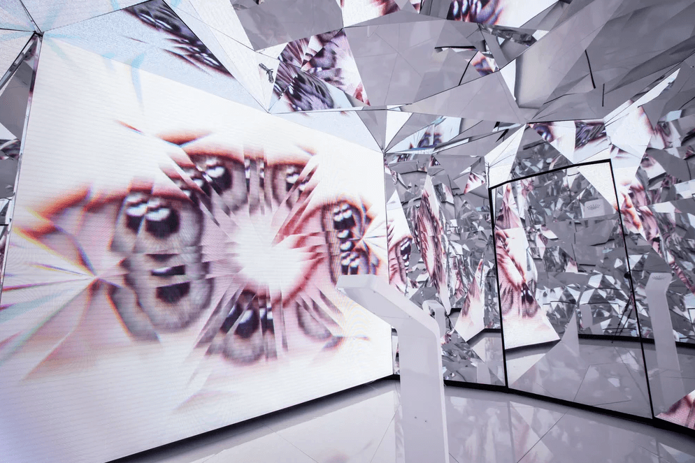Fragmented reflections of a face create an abstract kaleidoscope pattern across triangular mirror panels.