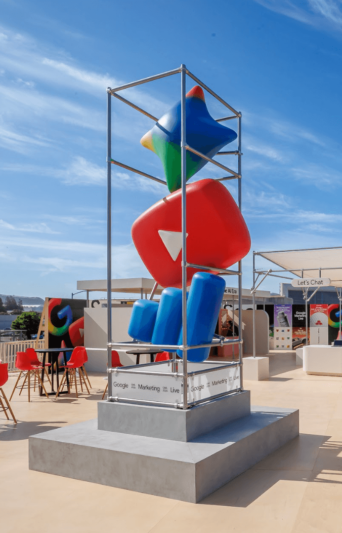 Tall outdoor sculpture of stacked red, blue, yellow, and green geometric shapes on a pedestal against a blue sky.