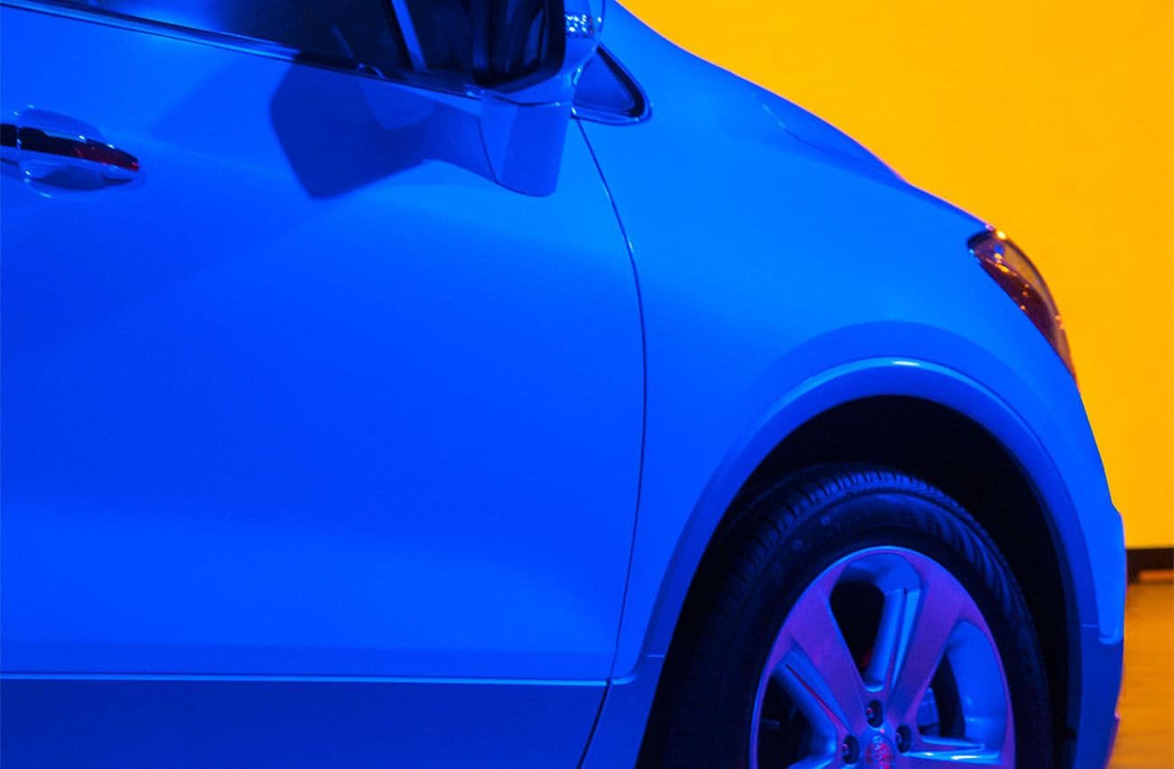 Close-up of a car's front fender and side mirror lit in blue against an orange background.