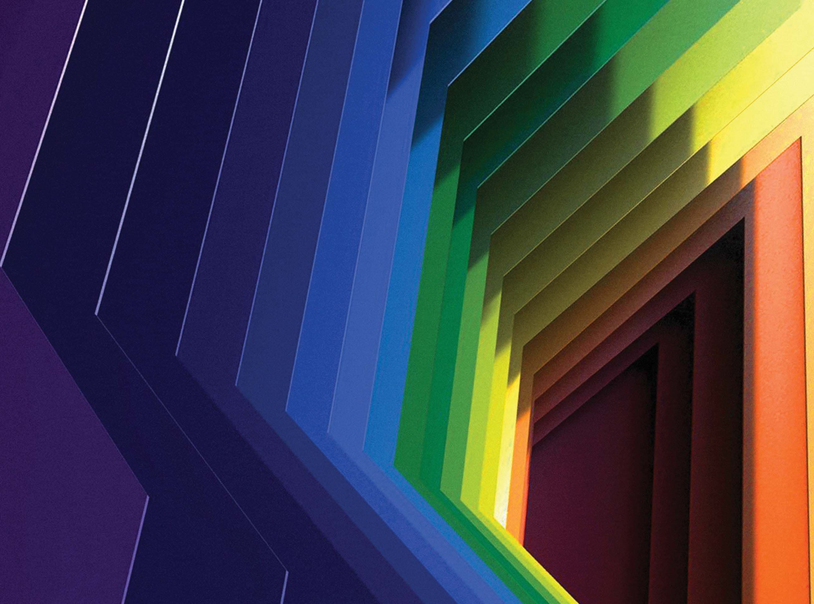 Angled rainbow-gradient folded panel wall viewed close up, transitioning from blue through green to orange.