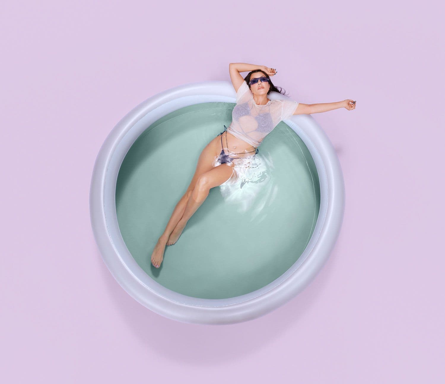 Overhead view of a woman lying in a teal circular tub.