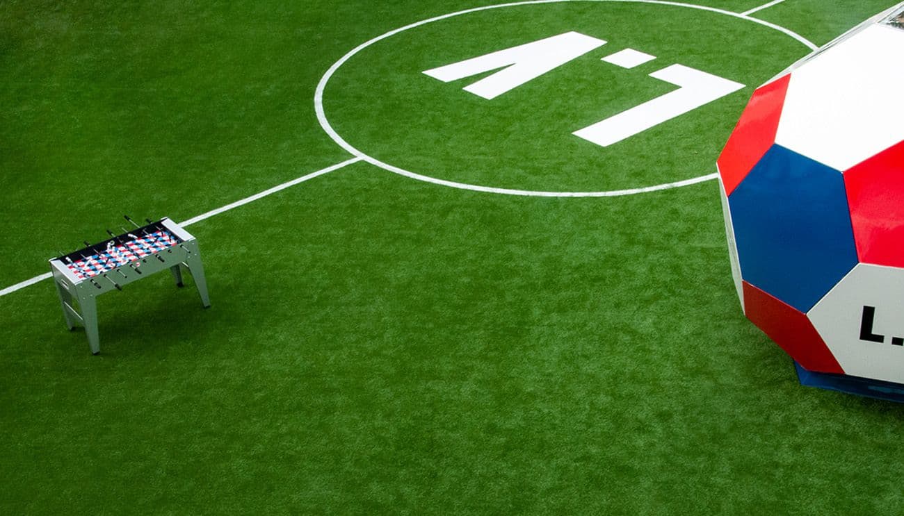 Foosball table and a giant Louis Vuitton monogram soccer ball set on artificial turf.