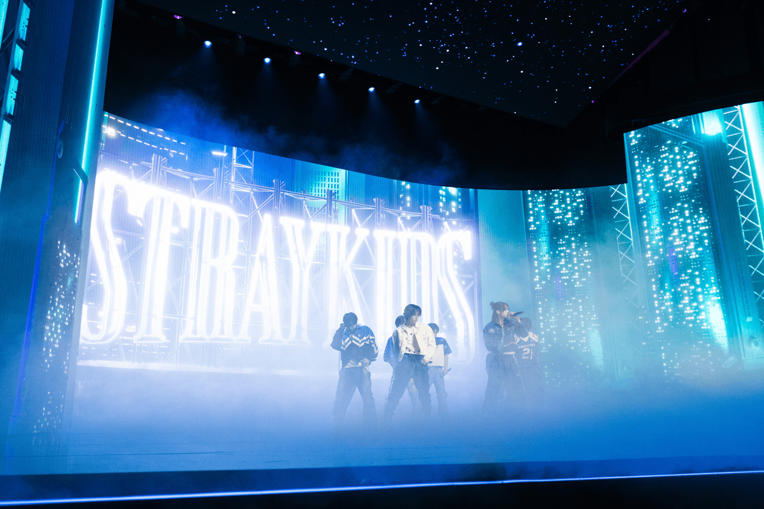 Stage screens displaying the text "STRAYKIDS" amid foggy blue lighting with performers below