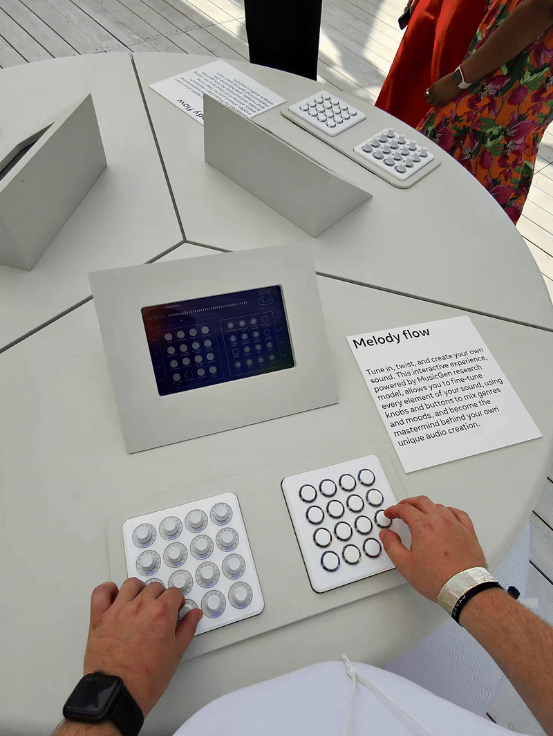 Overhead view of a person's hands operating circular knob panels next to a screen labeled 'Melody flow' on a round white interactive table.