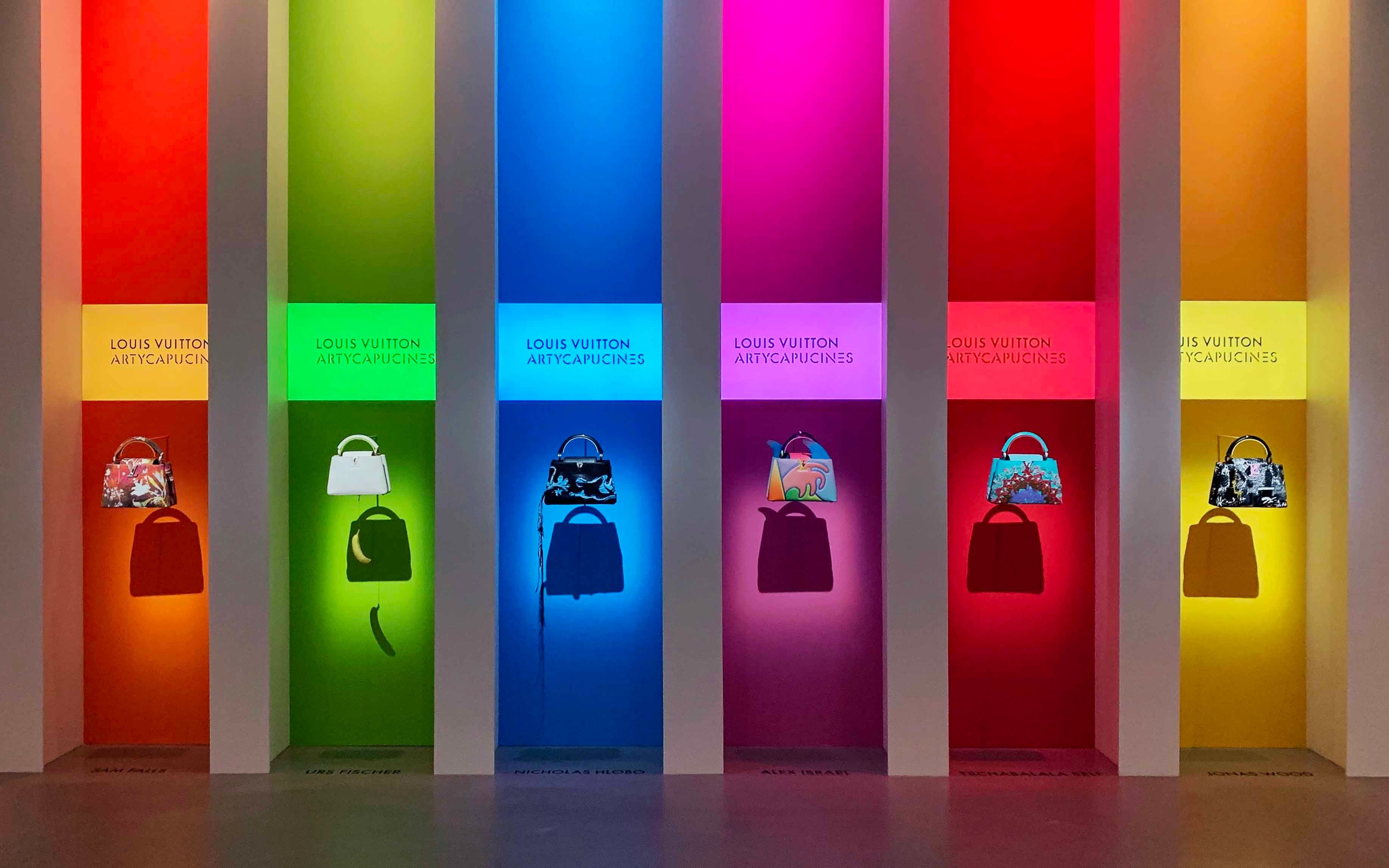 Row of colorful illuminated columns, each displaying a single handbag.