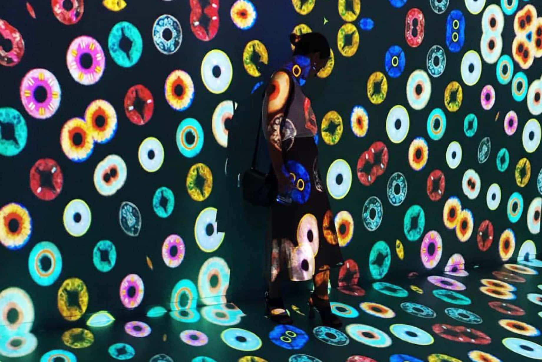 Person standing in an immersive room covered in colorful projected ring and eye-like patterns.