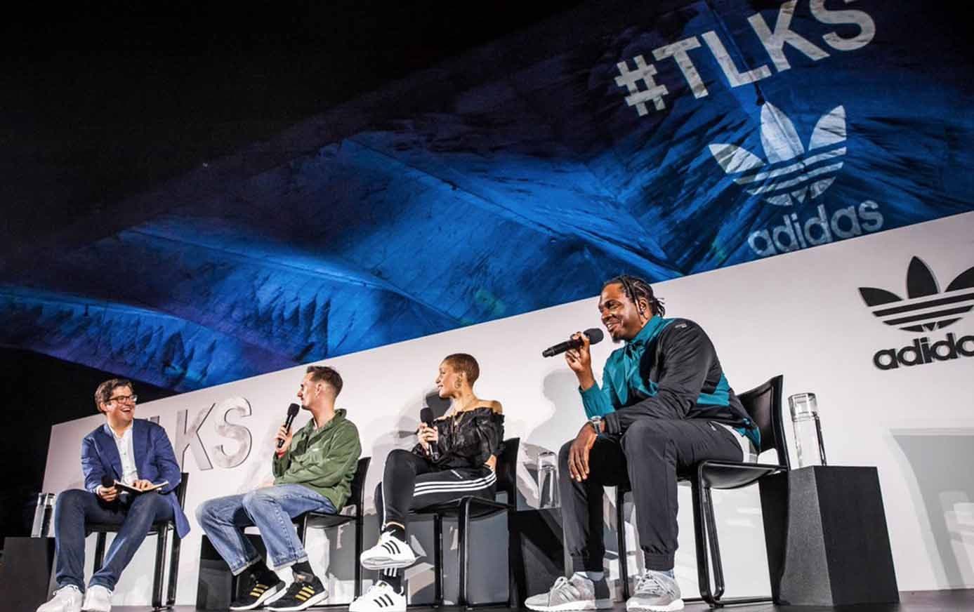 Four panelists seated on stage speaking into microphones under a blue-lit canopy, with #TLKS and adidas trefoil logos projected behind them.