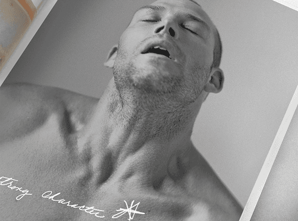 Close-up black-and-white photo of a shirtless bald man with eyes closed, with a handwritten caption reading "Strong Character" across his chest.