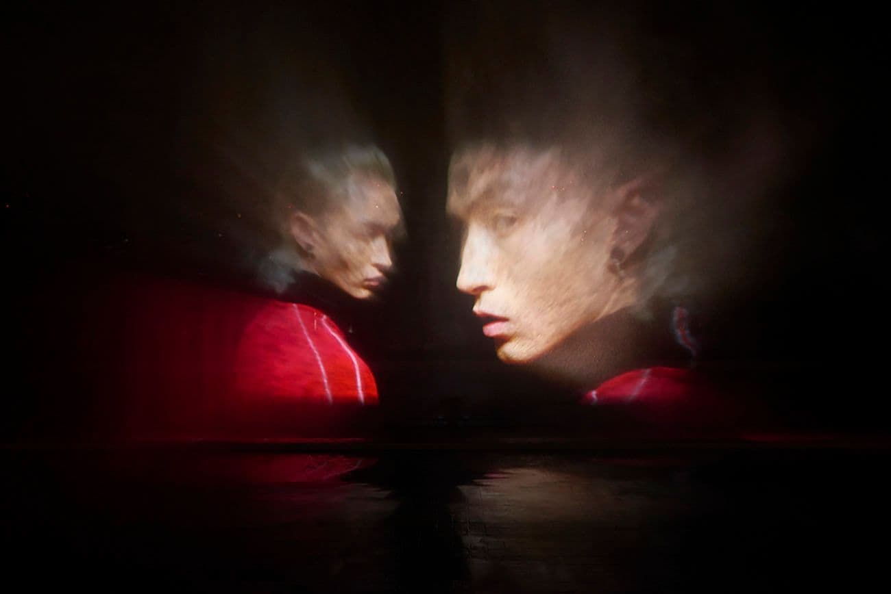 Two mirrored close-up profiles of a person's face lit in red against a dark background.
