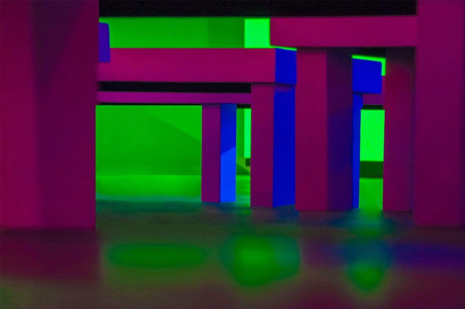 Close-up of bench and table legs lit in pink and green neon light with reflective puddles on the floor.