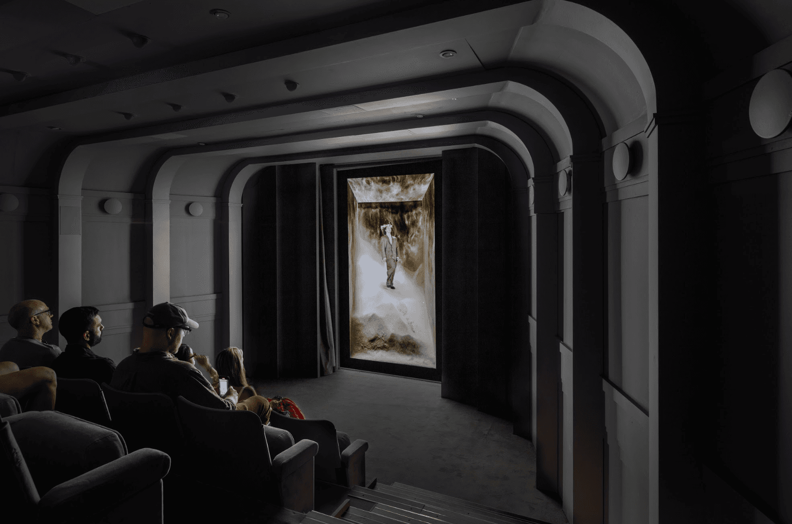People seated in a dark theater watching a nature scene projected on a large screen framed by an arched tunnel corridor.