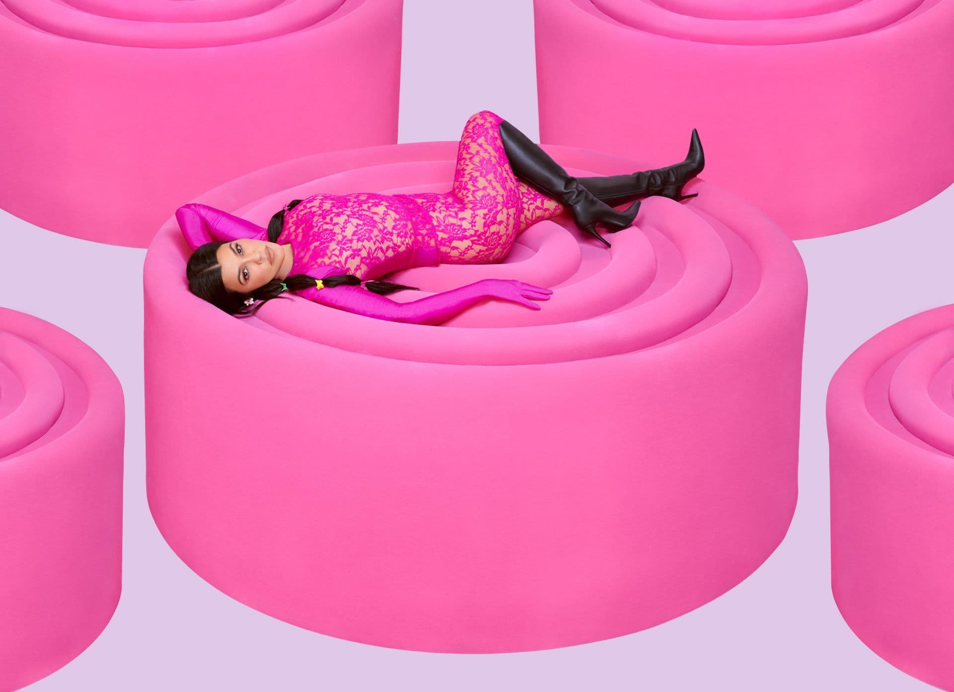 Woman in a pink outfit reclining across a large pink sculptural pedestal.