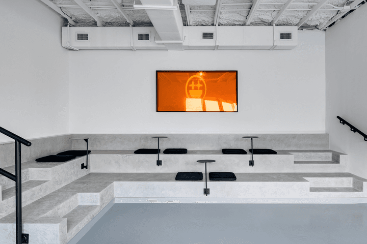 Tiered concrete seating with black cushions facing a wall-mounted screen glowing orange