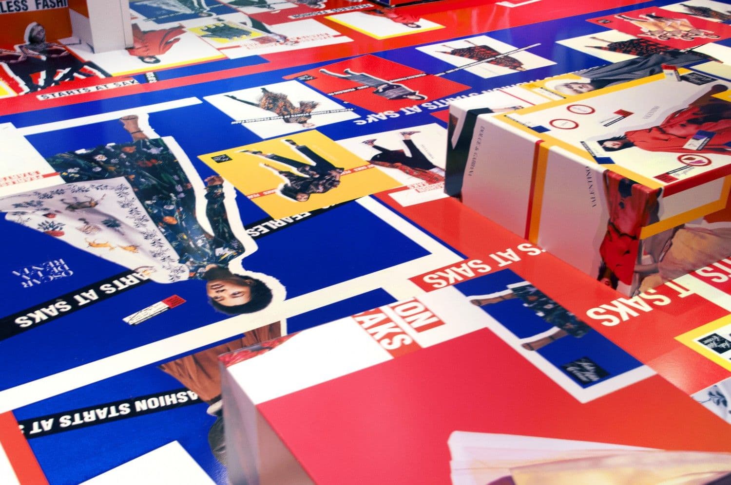 Table displaying fashion campaign posters and postcards in red, white and blue Saks branding.