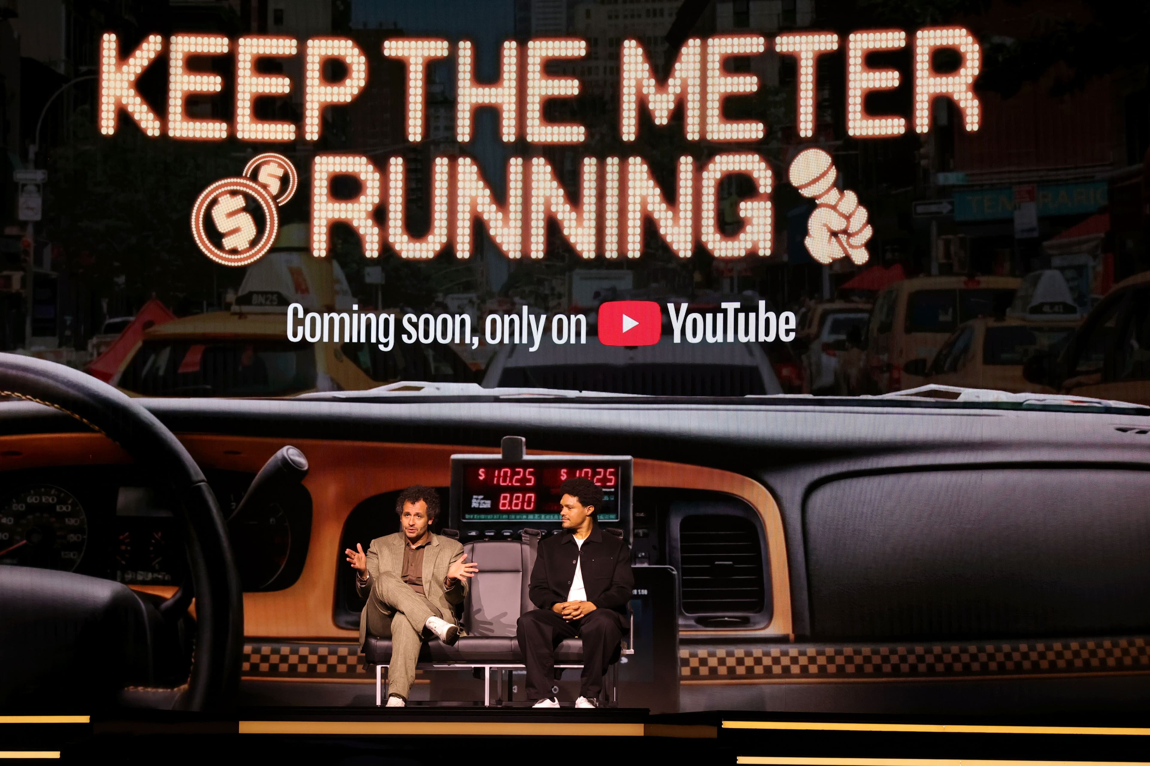 Stage screen reading "KEEP THE METER RUNNING, Coming soon, only on YouTube" above a taxi-cab set with two seated hosts