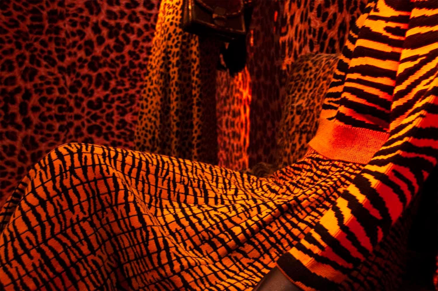 Close-up of leopard and tiger-print fabric draped over a bench in an orange leopard-print room.