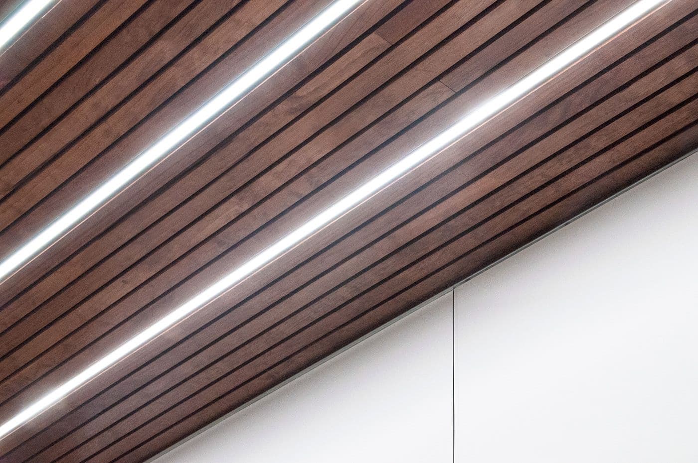 Close-up of an angled wood-slat ceiling with a recessed linear light strip.