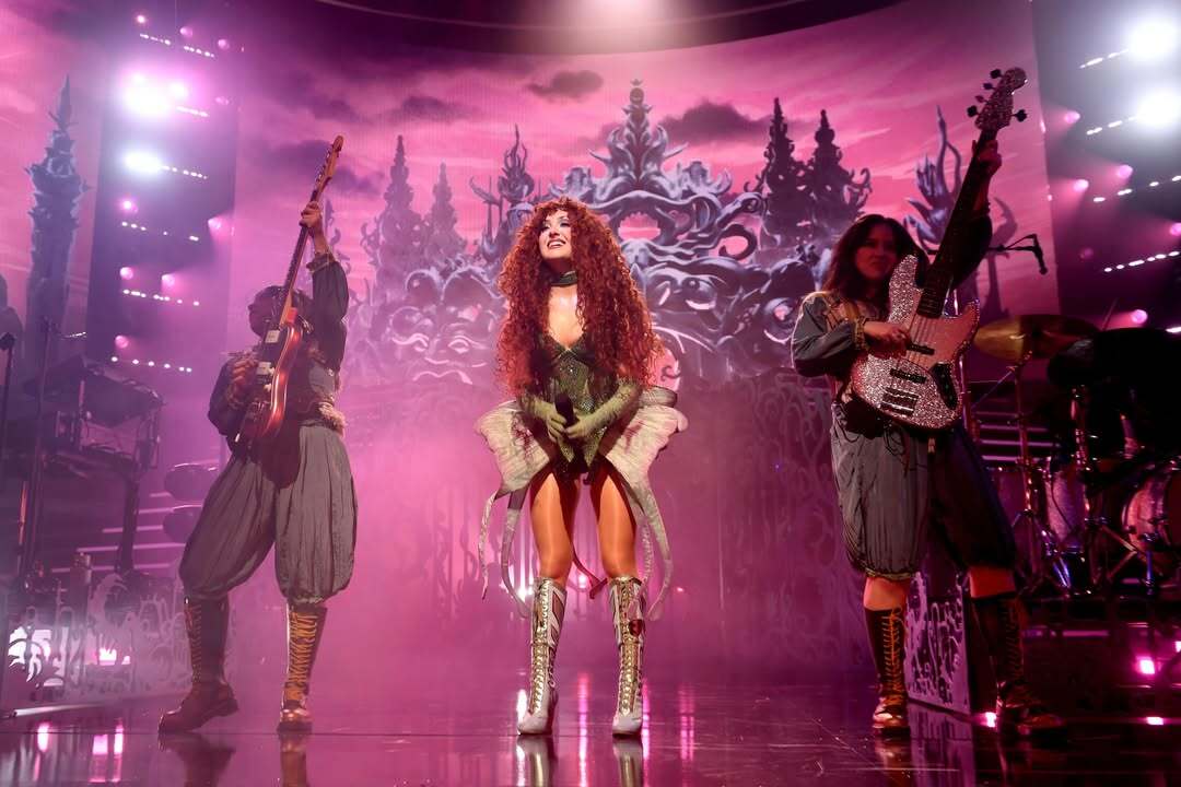 Three performers in silver warrior-style costumes descending a purple-lit stage staircase