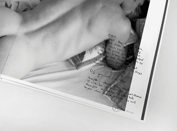 Close-up book page of a hand resting on bedding beside handwritten annotations.