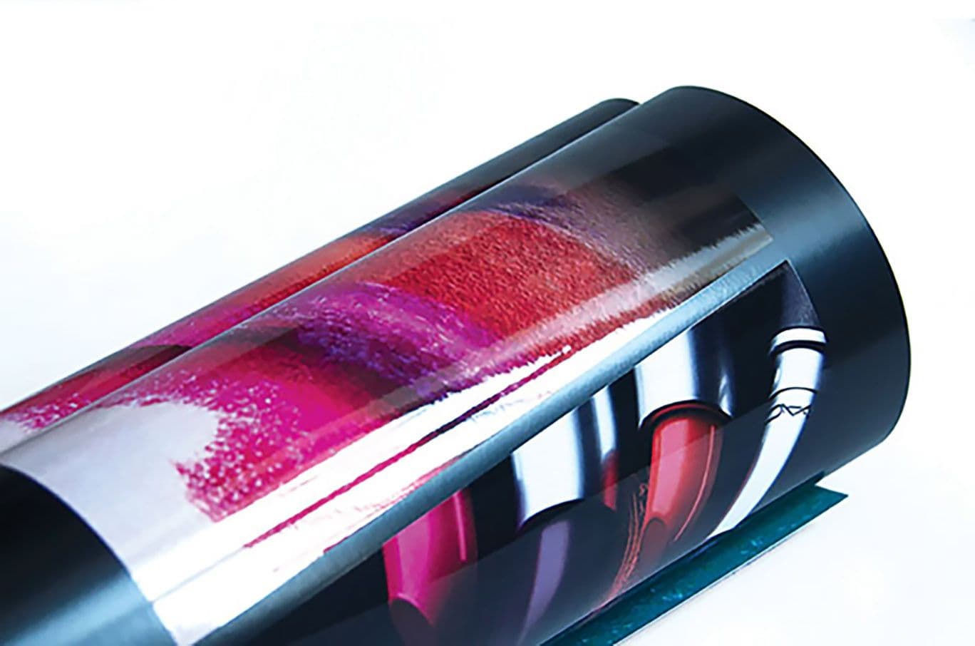 Rolled glossy print sample with a swirl of pink, red, and purple lipstick swatches reflected on its curved surface.