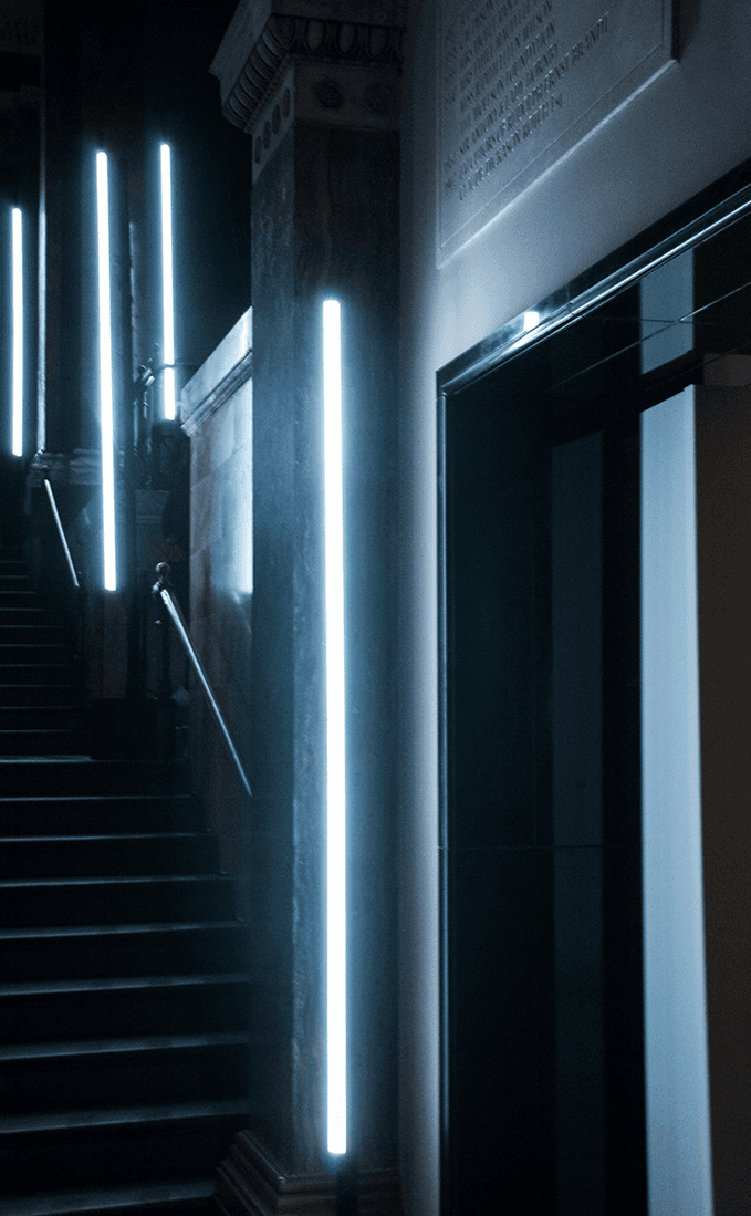 Vertical LED light strip mounted on a stone column beside a doorway, with a staircase in the background.