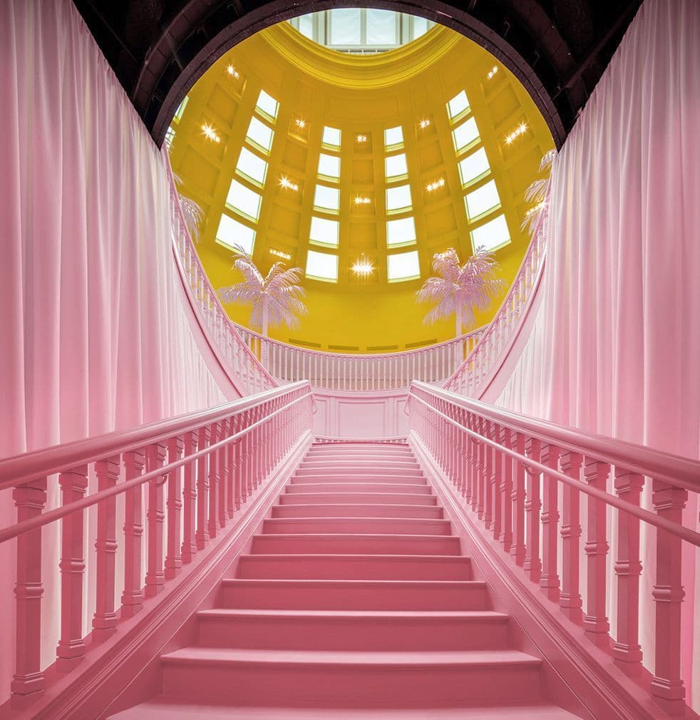 Pink spiral staircase rising toward a round yellow-lit skylight.