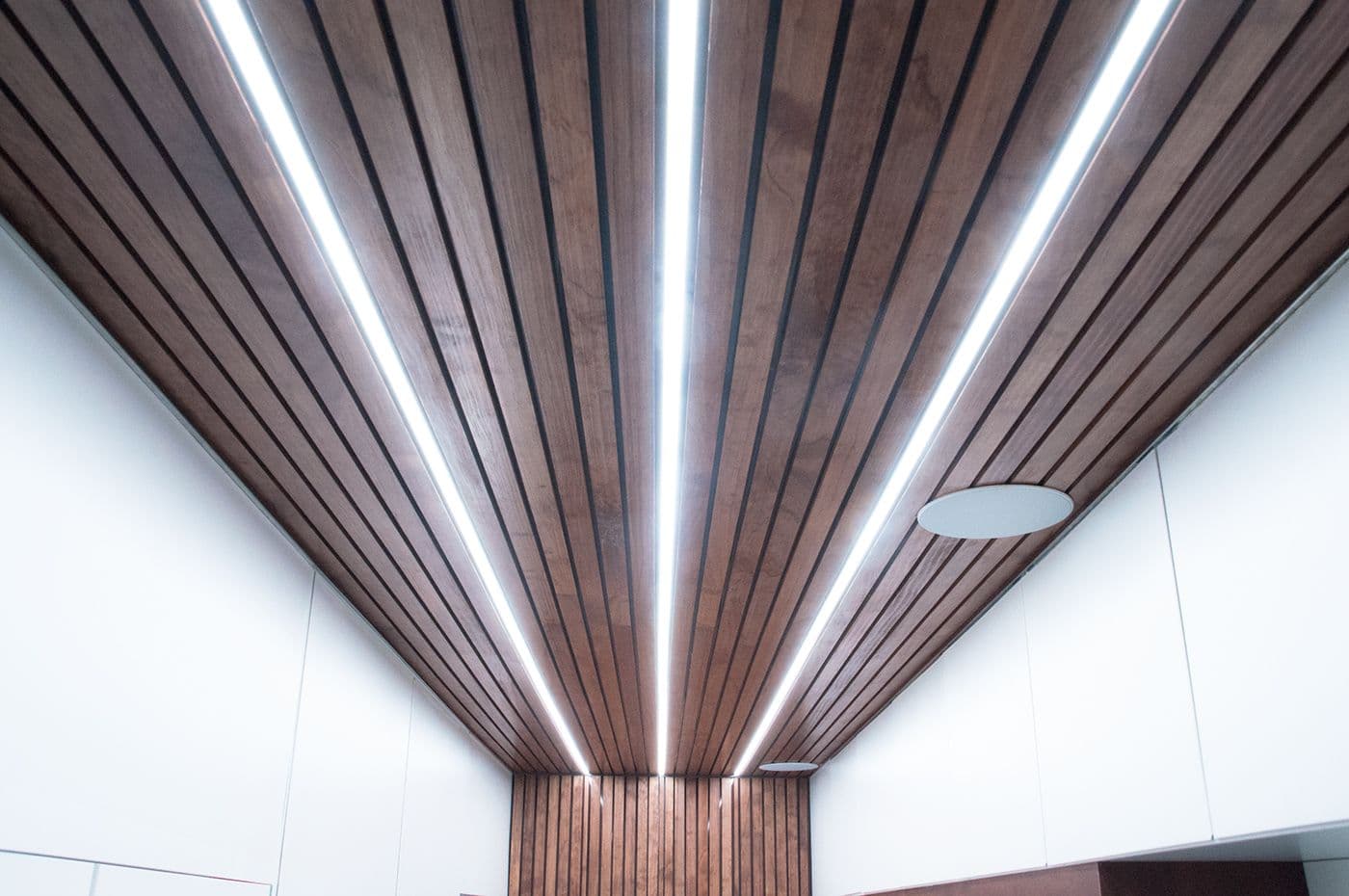 Interior ceiling detail of angled wood slats converging toward a linear light strip.
