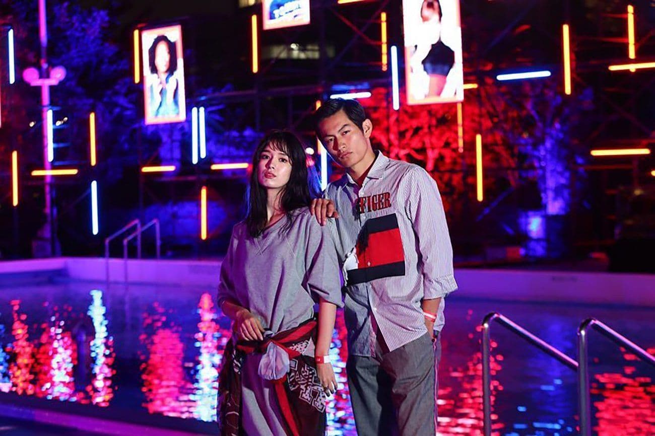 Woman and man standing together beside a reflecting pool at night, backed by illuminated portrait screens.