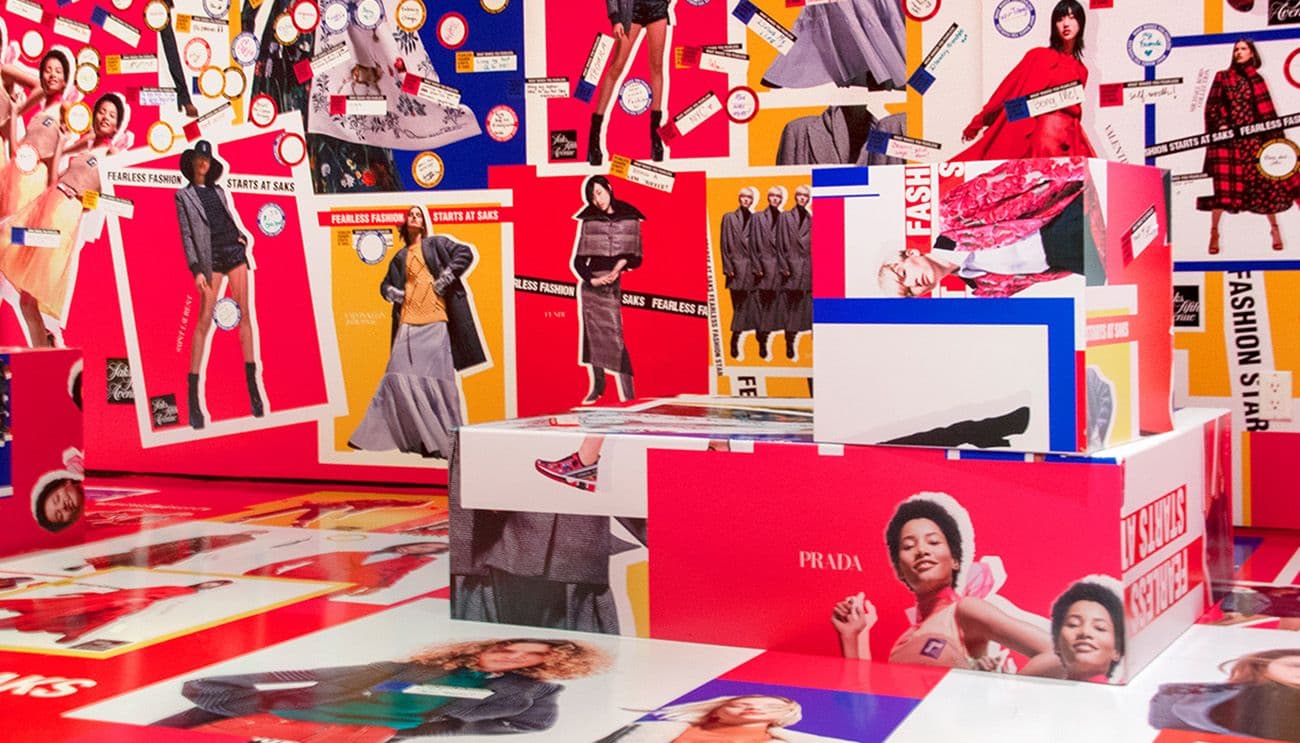 Room with walls and floor covered in red, white and blue fashion campaign graphics and "Fashion Starts At Saks" signage.