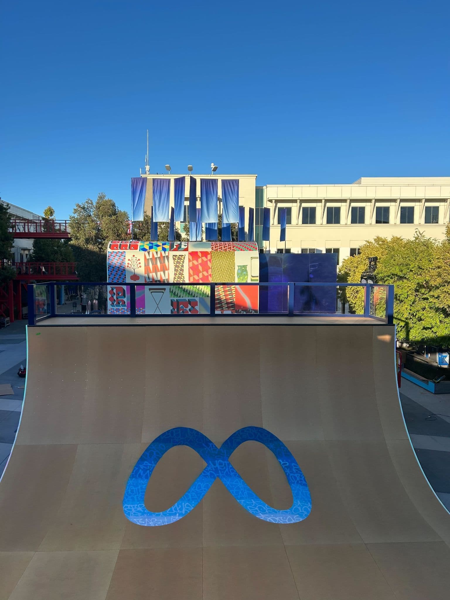 Outdoor skate ramp painted with the Meta infinity logo, backed by a colorful mural and building.