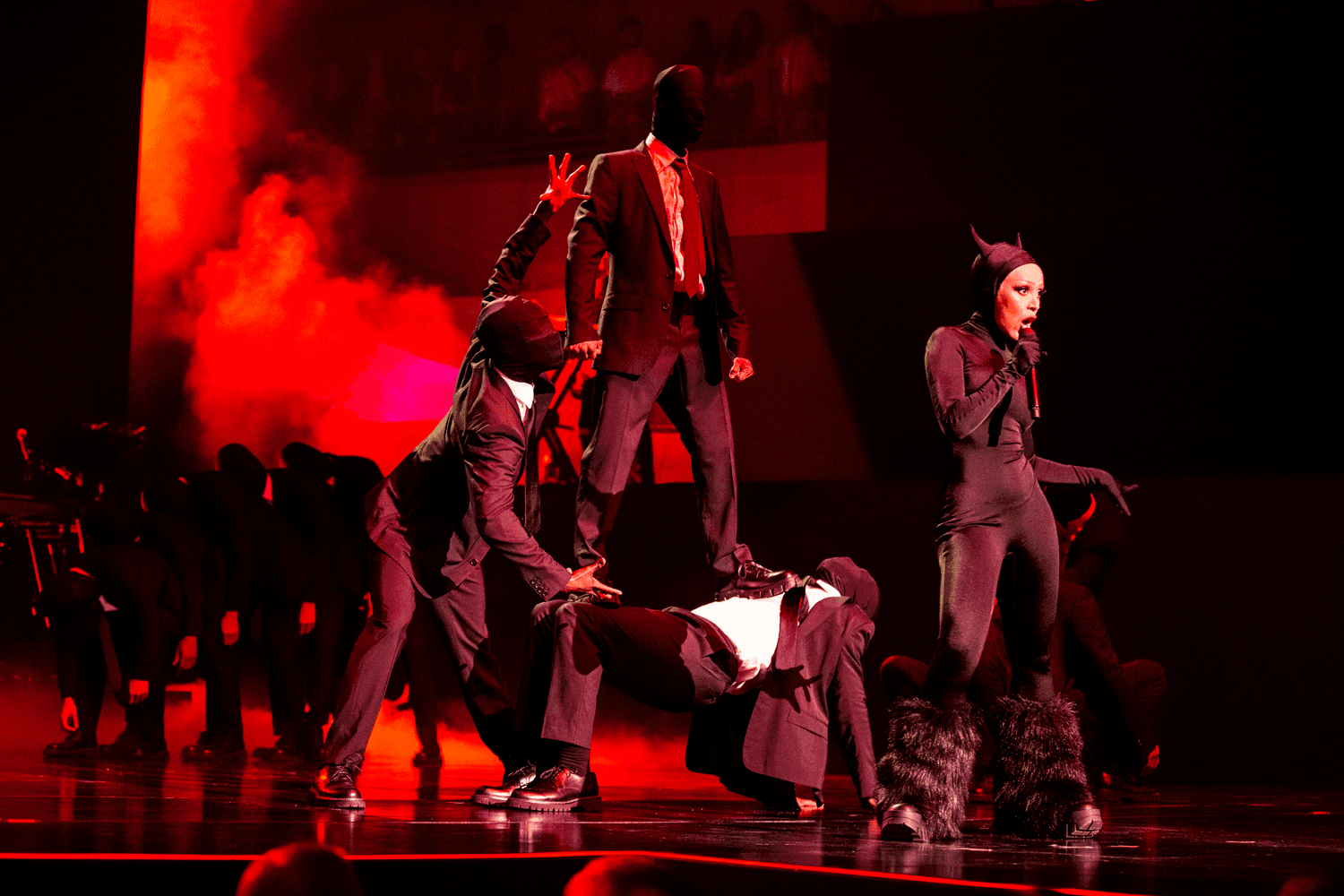 Group of dancers in dark tactical-style outfits performing with red smoke on stage
