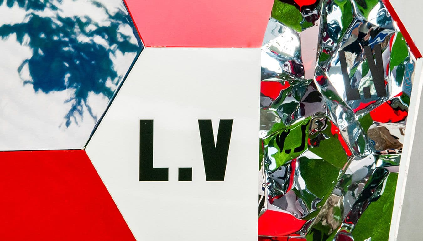 Louis Vuitton monogram-patterned soccer ball on artificial turf beside a branded number seven marking at center pitch.