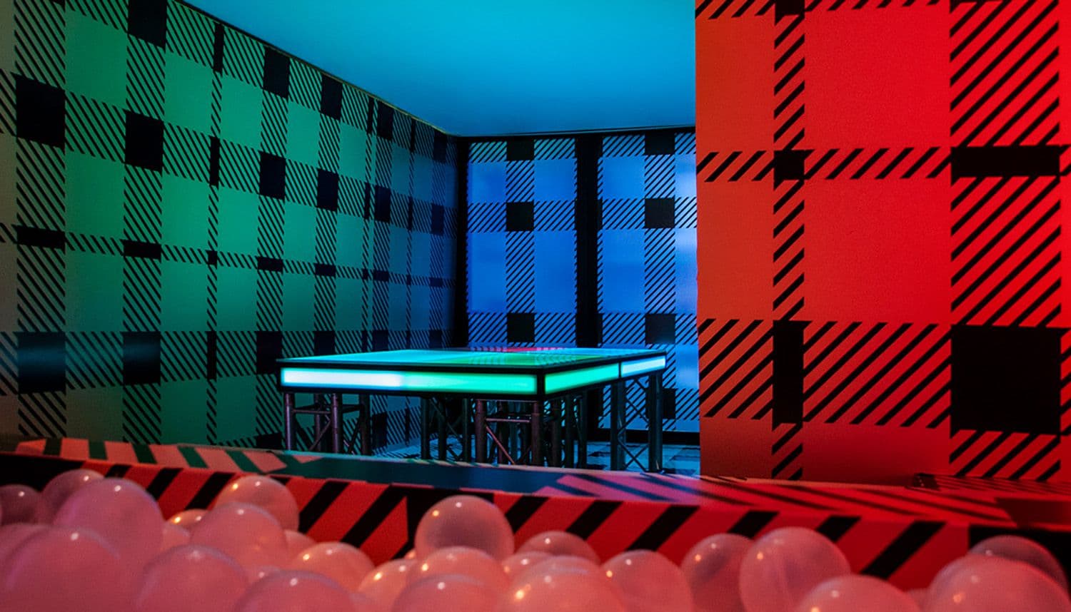 Corner of a room with red and green plaid walls, a glowing table, and red balloons in the foreground.