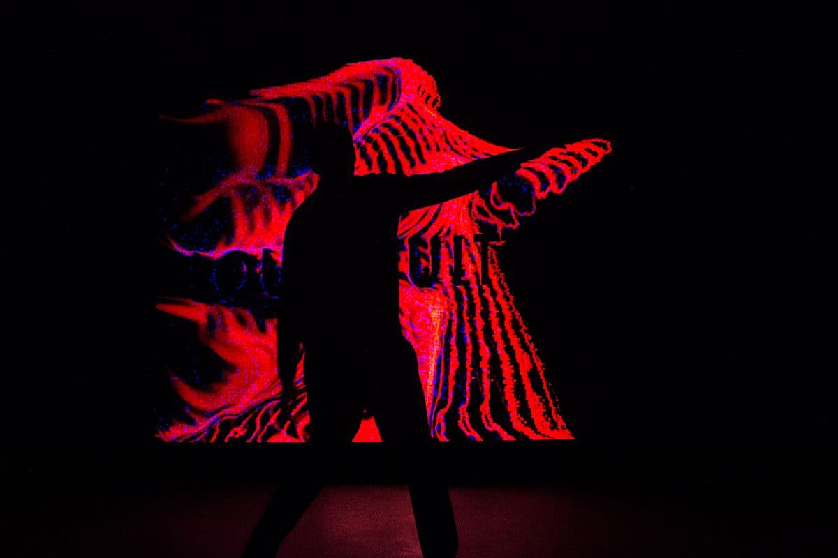 Silhouette of a dancer against a red light projection with rippling wave-like patterns.