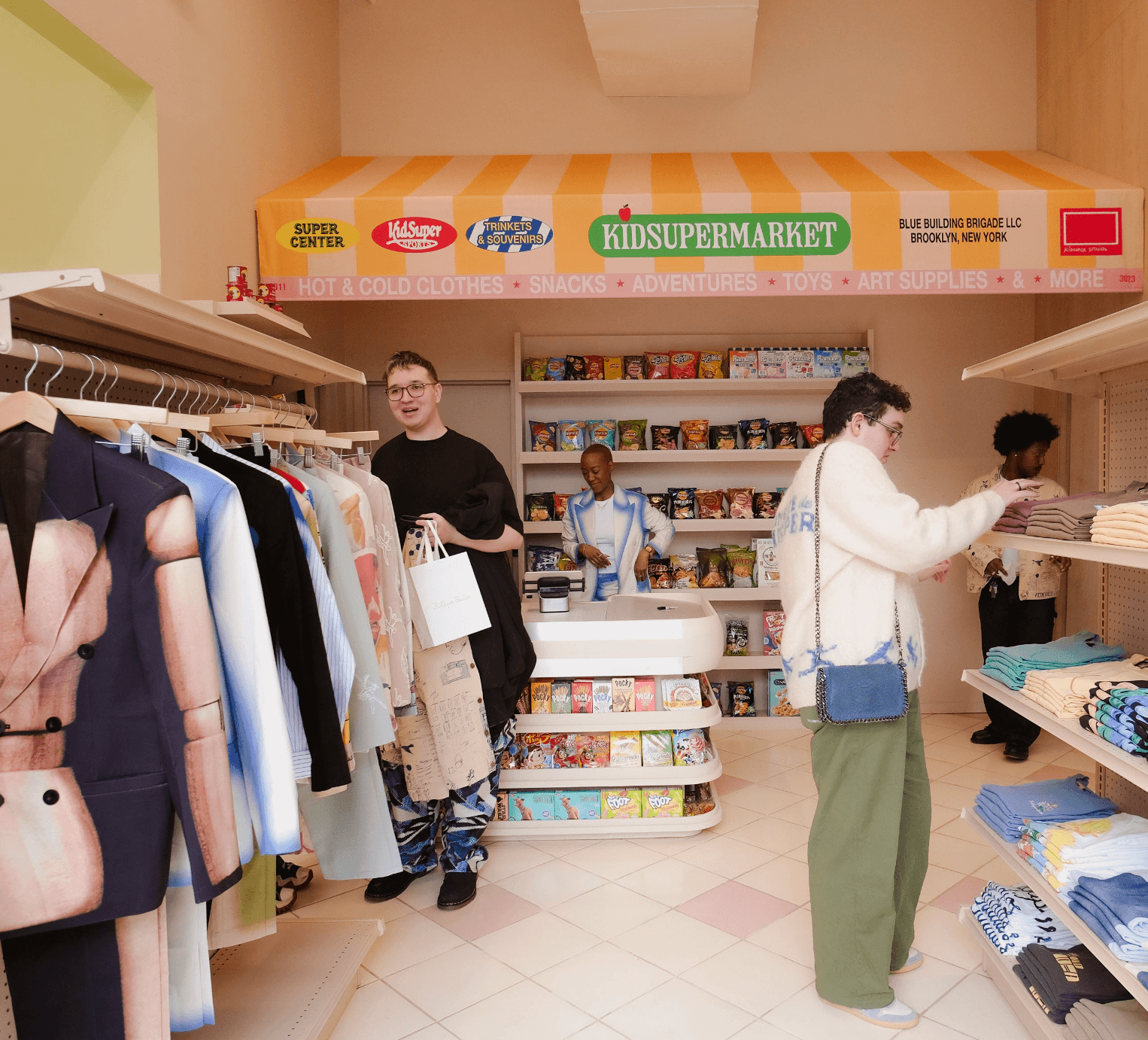 Store interior with orange Kidsupermarket signage above racks of clothing as shoppers browse
