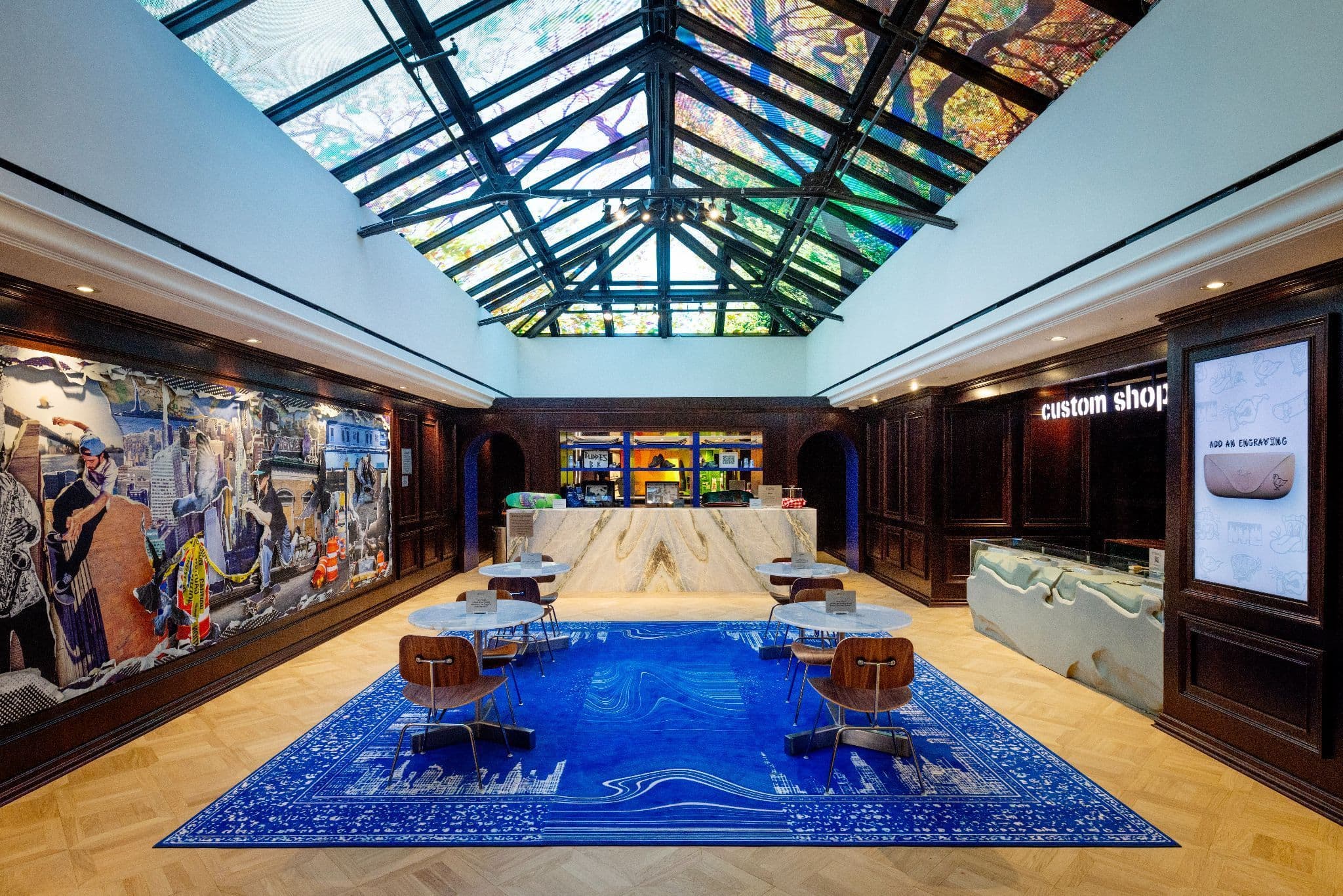Retail room with a skylight painted with an illustrated mural, a central table on a blue wave-patterned rug, and dark wood wall cases.