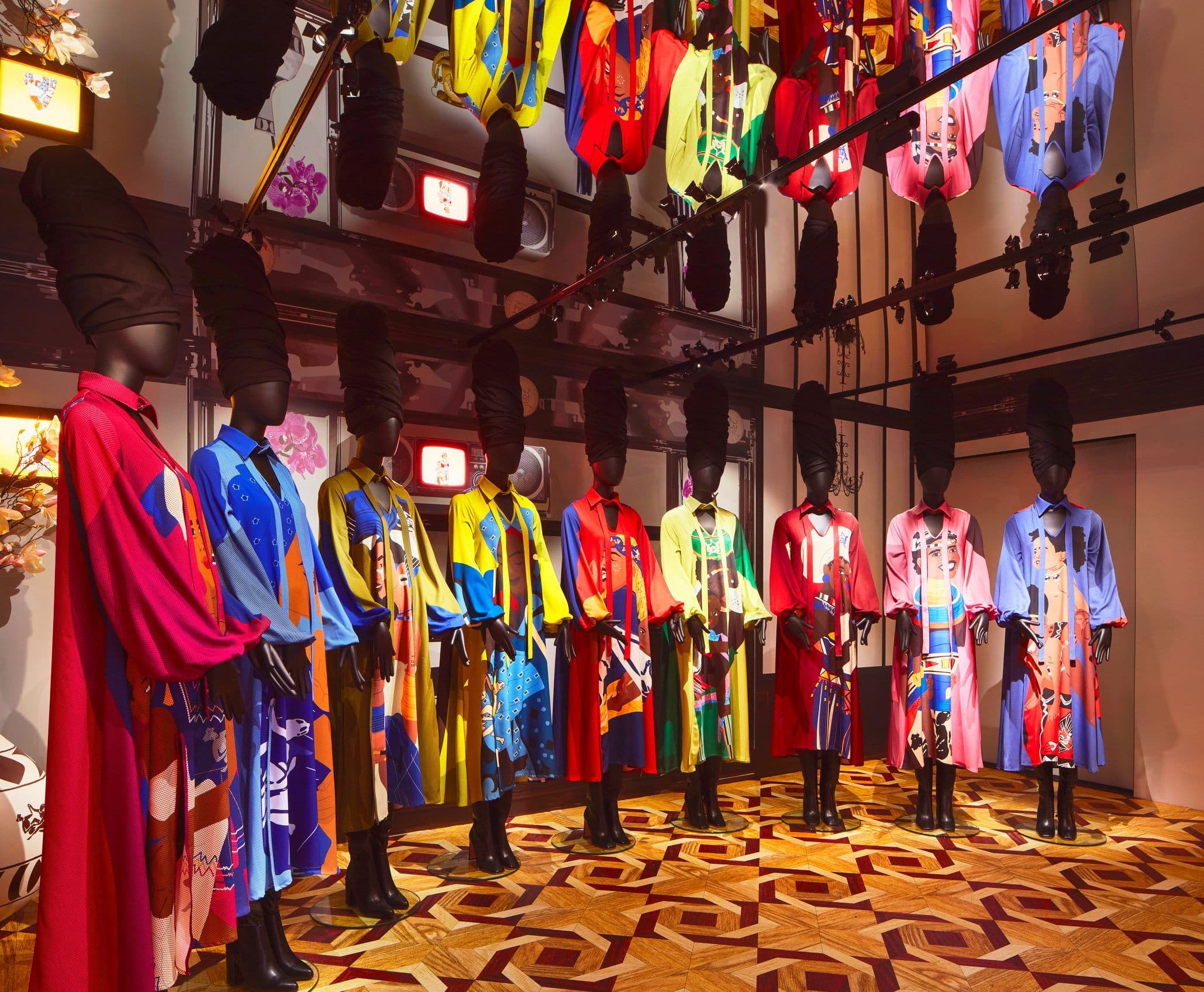Rack of colorful printed garments on mannequins in a room with a patterned rug.