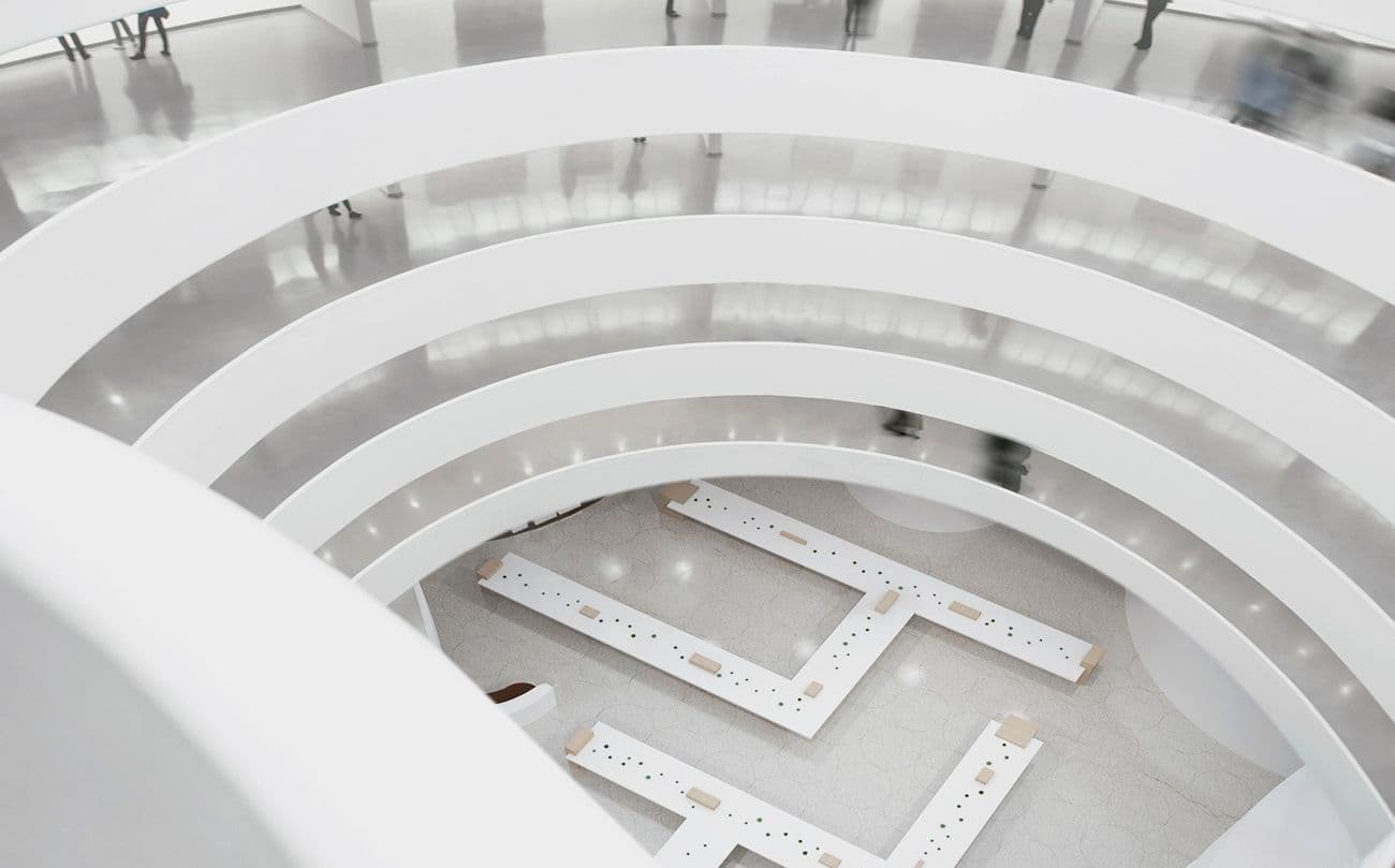 Aerial view down the Guggenheim Museum's spiral atrium with a geometric wooden bench installation on the ground floor and blurred figures walking