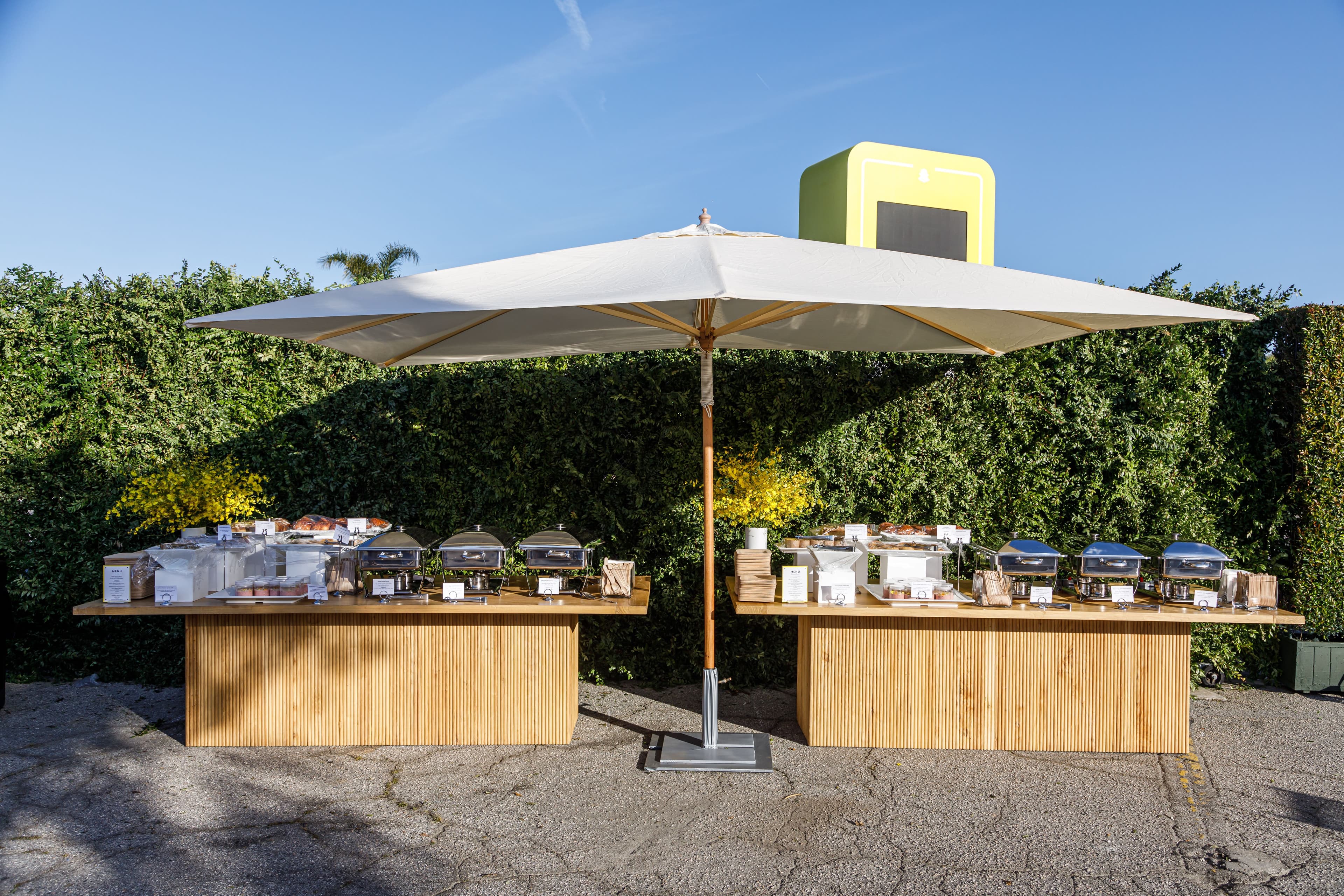Outdoor catering table with a large umbrella and food spread.