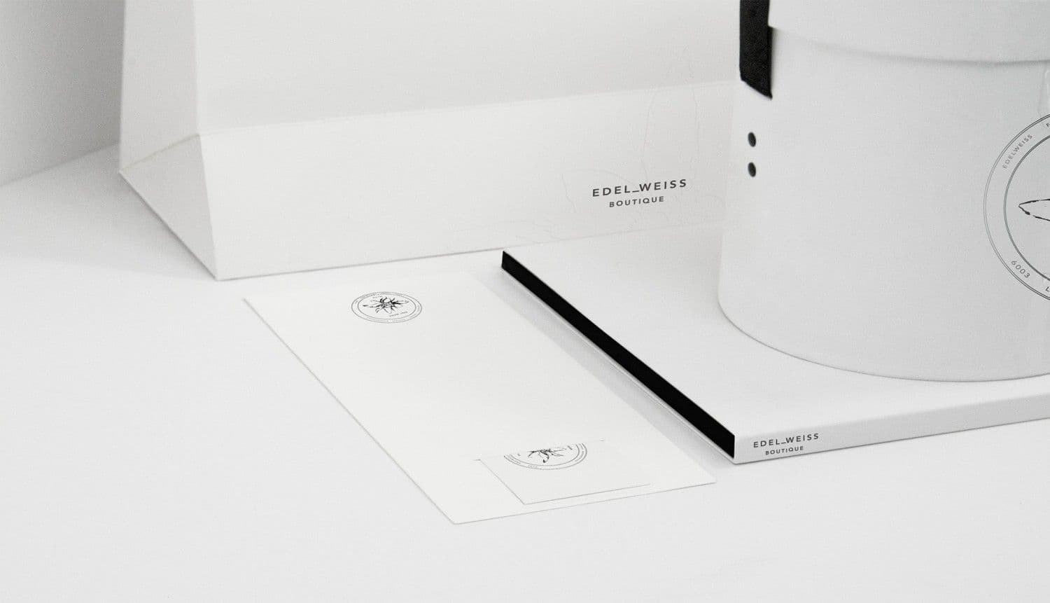 White paper bag, letterhead with a wing emblem, and a rolled cylindrical box arranged together on a white surface.
