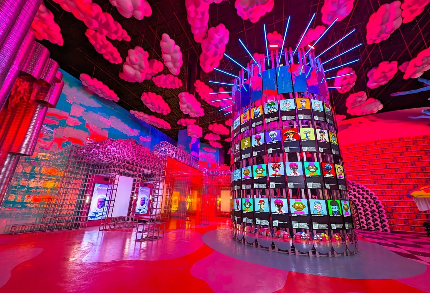 A cylindrical LED video tower surrounded by pink cloud decorations hanging from the ceiling in a red-lit room.