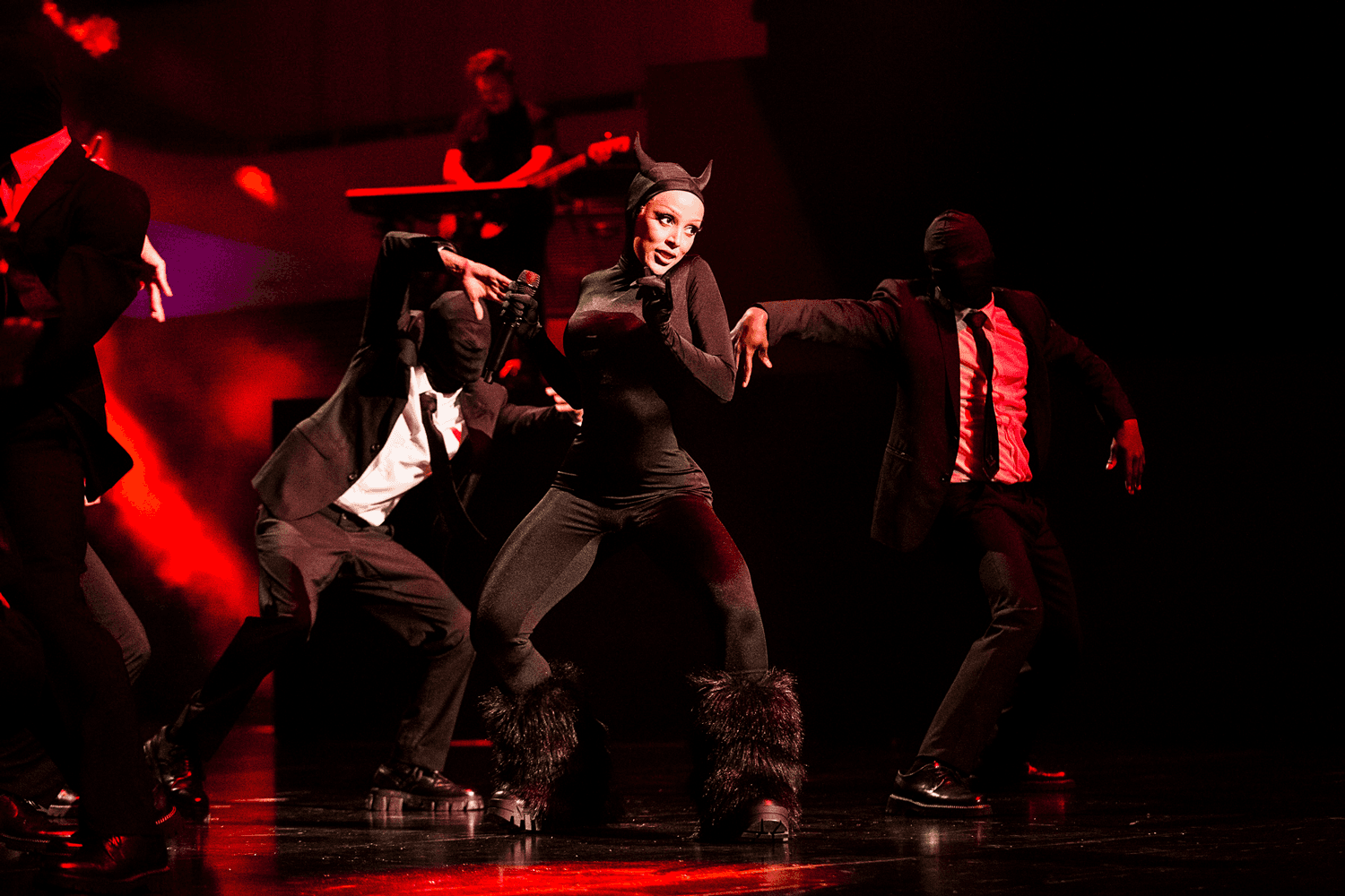 Group of dancers in dark outfits performing a choreographed routine on stage.