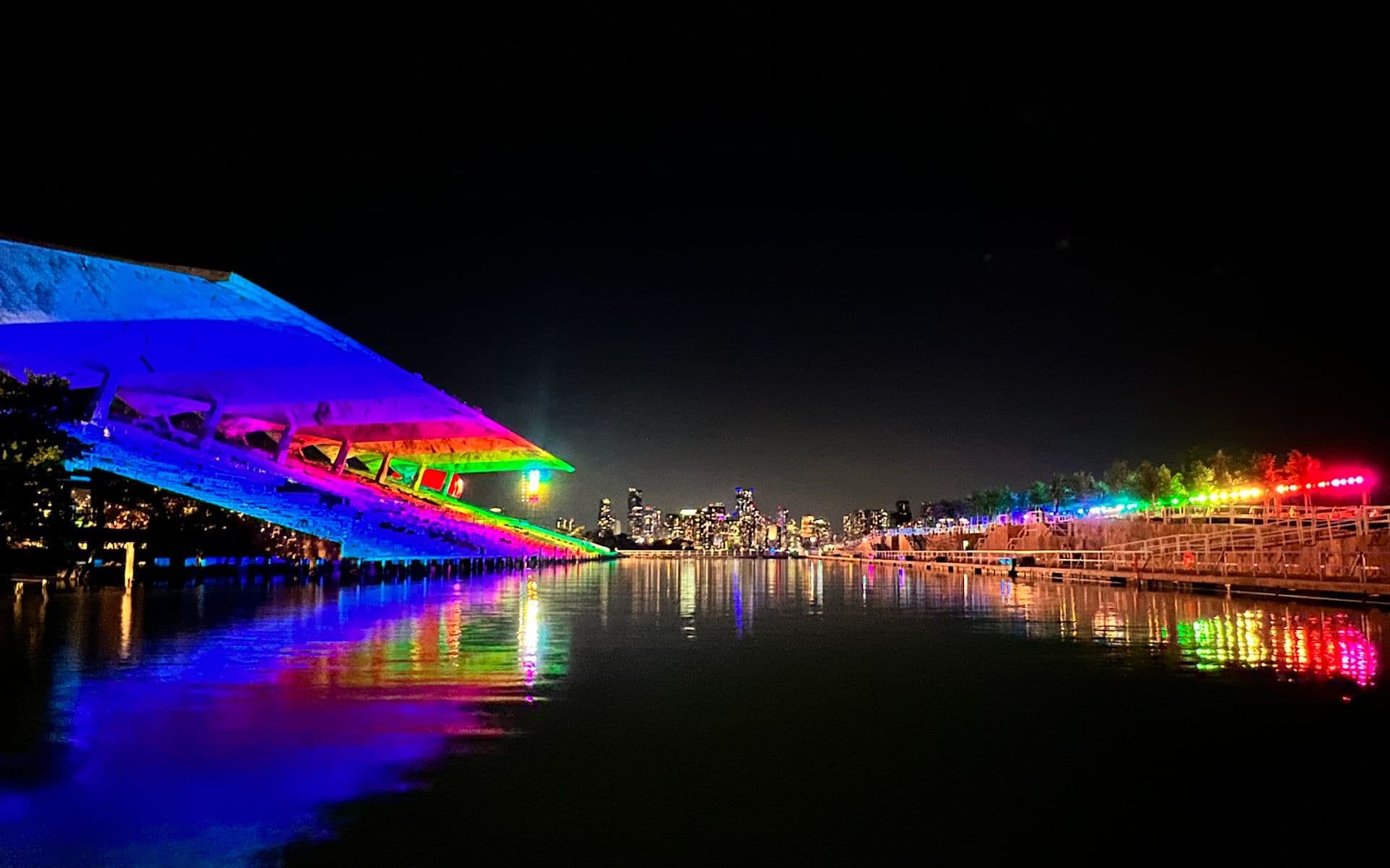 Close-up view of the rainbow-lit dome installation glowing against the night sky, framed by trees