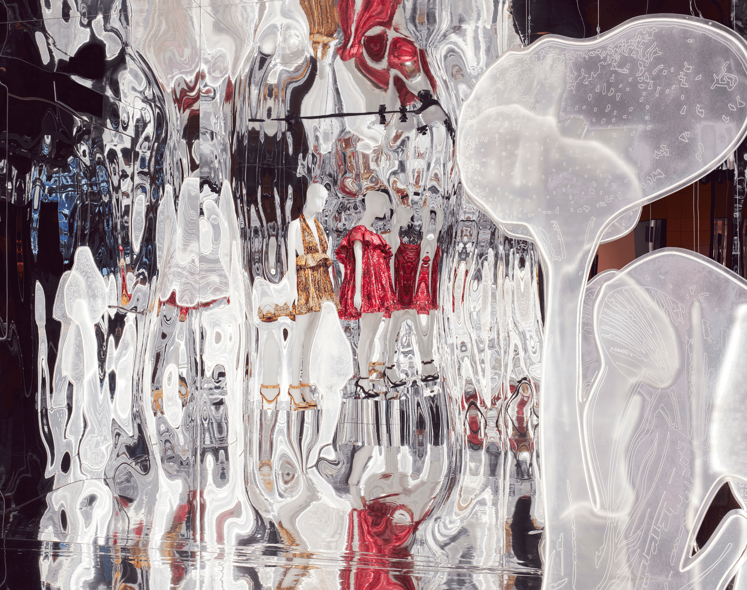 Close-up of a mirrored installation showing translucent white forms and red garment pieces reflected across the panels.